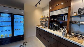 A modern kitchen with a coffee machine, shelves with jars, and a refrigerator displaying various items.
