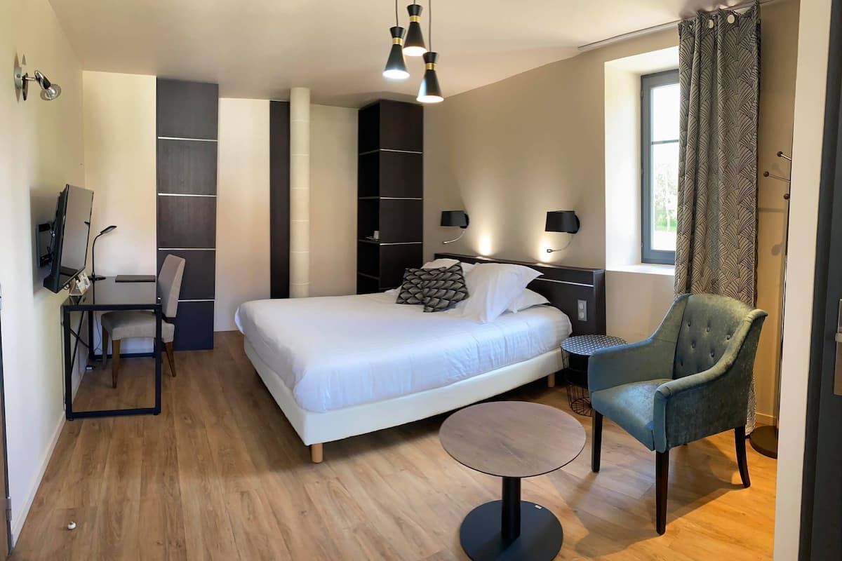 A modern hotel room with a large bed, a desk, a chair, and a small round table.