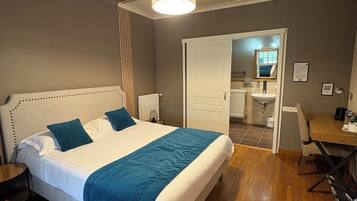 Un dormitorio con cama, mesitas de noche, escritorio y un baño visible a través de una puerta abierta.