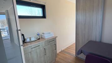Een moderne, compacte kamer met een kitchenette, een klein raam, een schuifdeur en een paarse stoel.