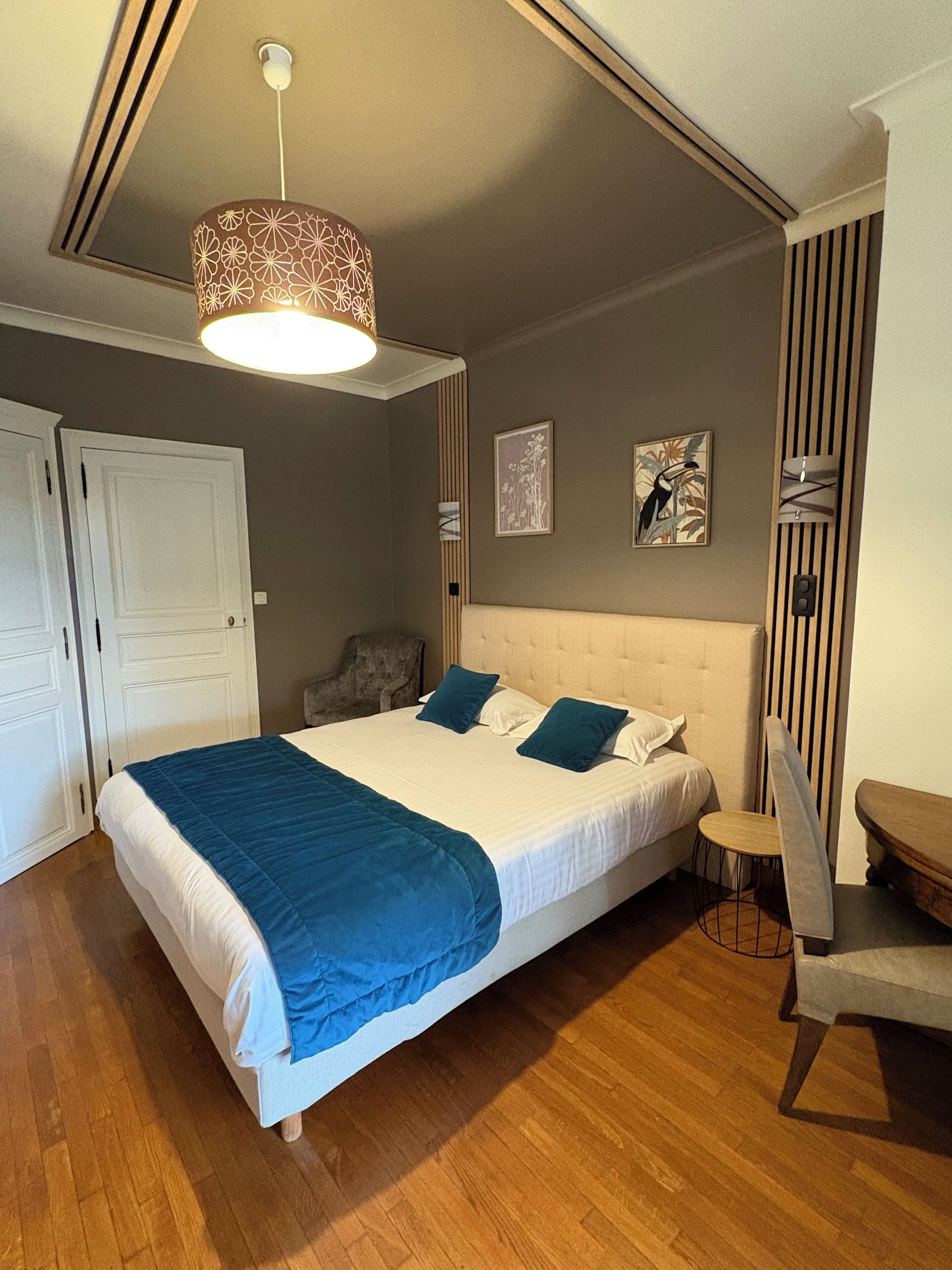 Une chambre à coucher avec un grand lit, une chaise, un bureau et un luminaire suspendu.