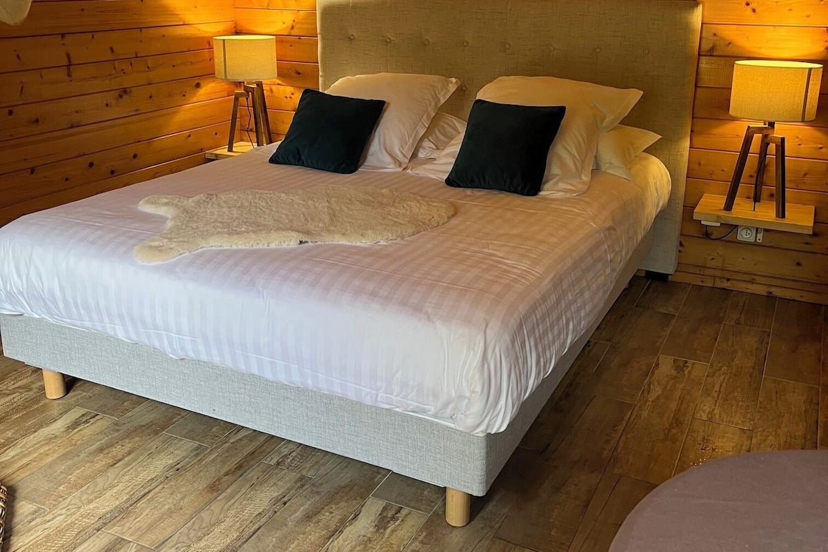 A wooden cabin-style bedroom with a bed, two bedside lamps, and a ceiling light.