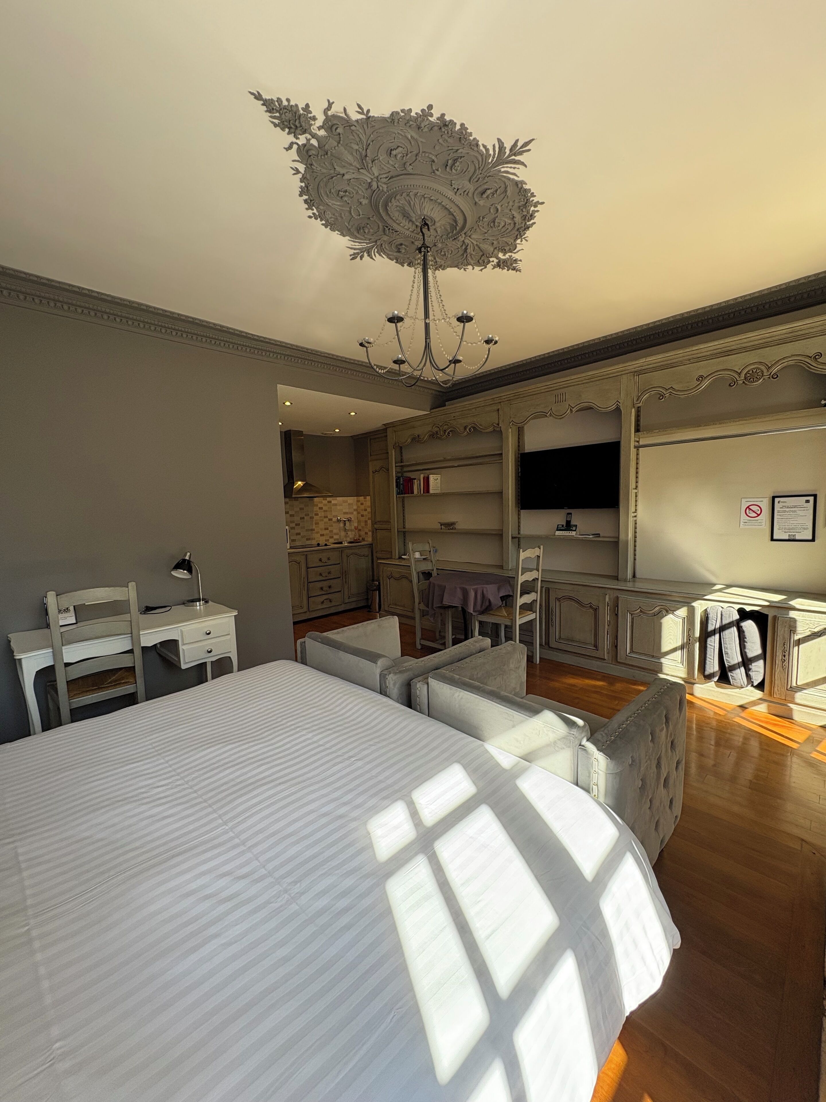 A bedroom with a large bed, a desk, a chair, a chandelier, and a wardrobe.
