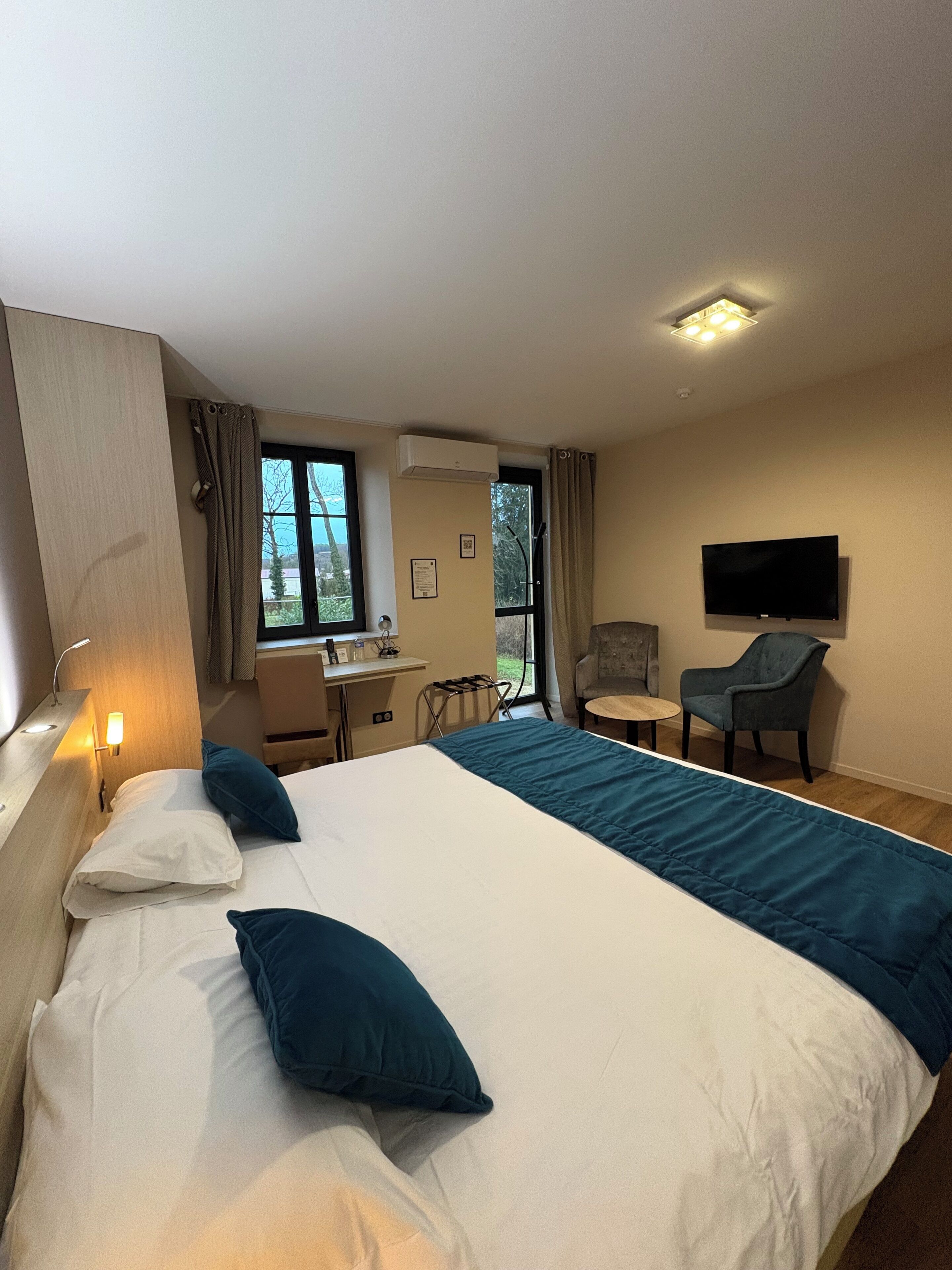 A hotel room with a large bed, a desk, a chair, a TV, and a window.