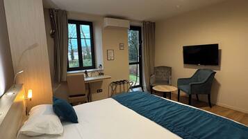 A hotel room with a large bed, a desk, a chair, a TV, and a window.