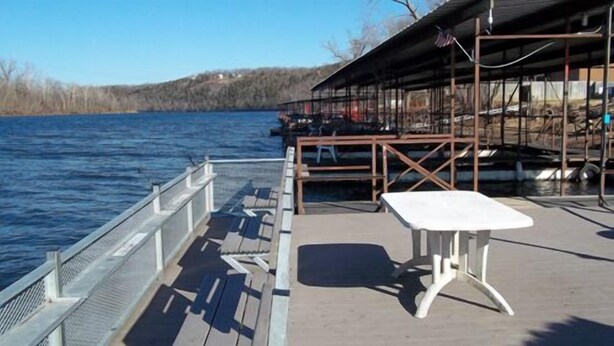 A dock with a table and chairs, overlooking a body of water with a building in the background. - Taneycomo Lakefront Resort (Branson)