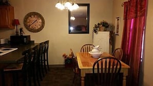 A dining area with a wooden table, chairs, a clock, a mirror, and a window with curtains. - Taneycomo Lakefront Resort (Branson)