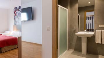 Een moderne hotelkamer met een houten vloer, een grote spiegel, een aan de muur bevestigde televisie en een aparte badkamer met wastafel en handdoekhouder.