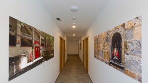 Un pasillo con suelo de baldosas, puertas de madera y dos paredes decoradas con cuadros enmarcados.