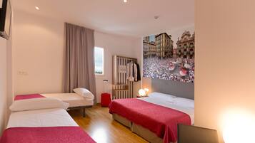 Habitación de hotel con dos camas, una maleta roja, un televisor montado en la pared y un cartel grande de un evento concurrido.