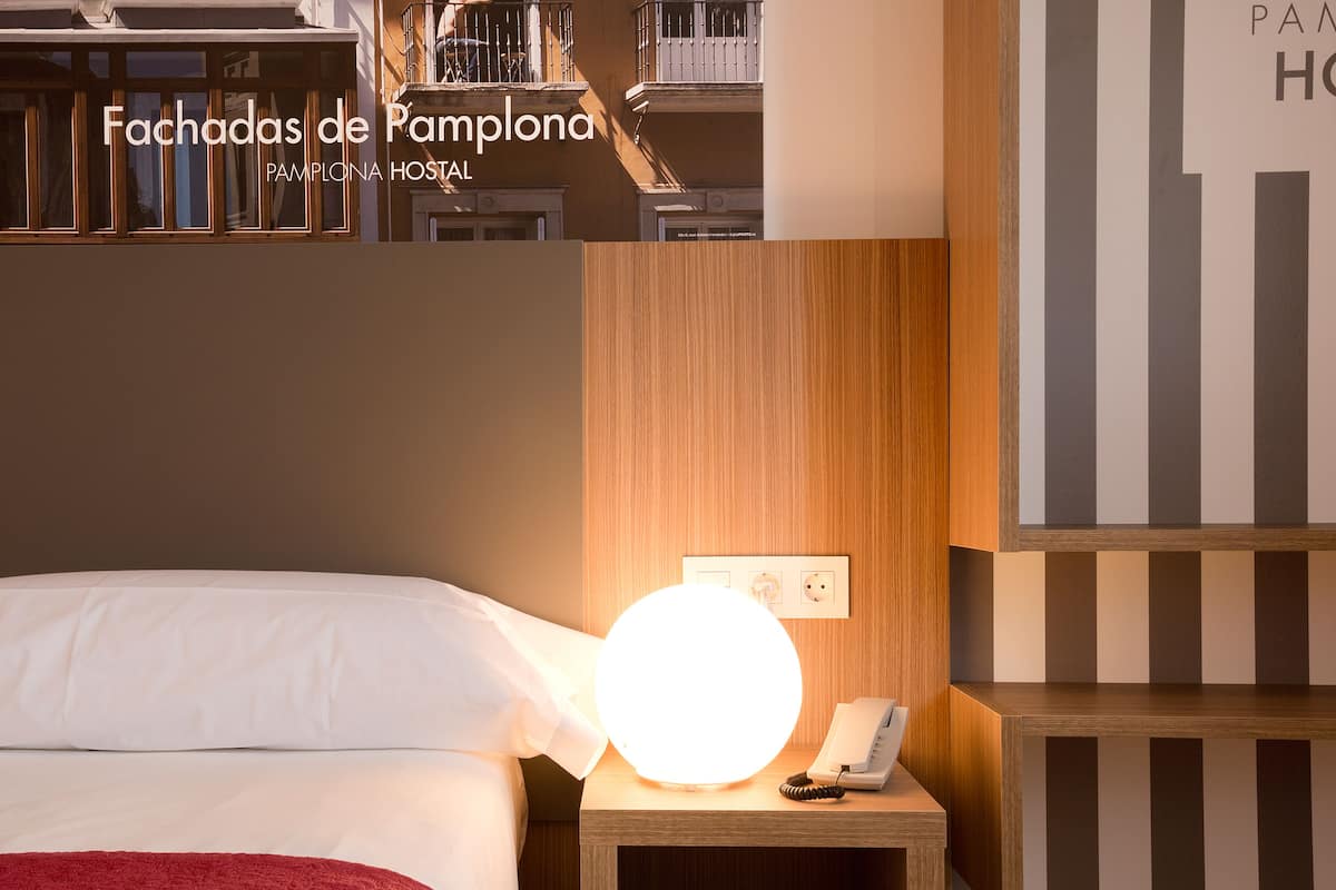 Een hotelkamer met een bed, een nachtkastje met een lamp en een aan de muur bevestigde telefoon.