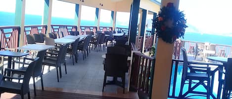 An outdoor dining area with tables and chairs, a ceiling fan, and a view of the ocean.