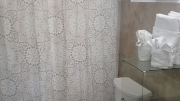 Kylpyhuone, jossa on kuviollinen suihkuverho, wc-istuin, lasinen suihkuseinä ja pyyheteline, jossa on pyyhkeitä.