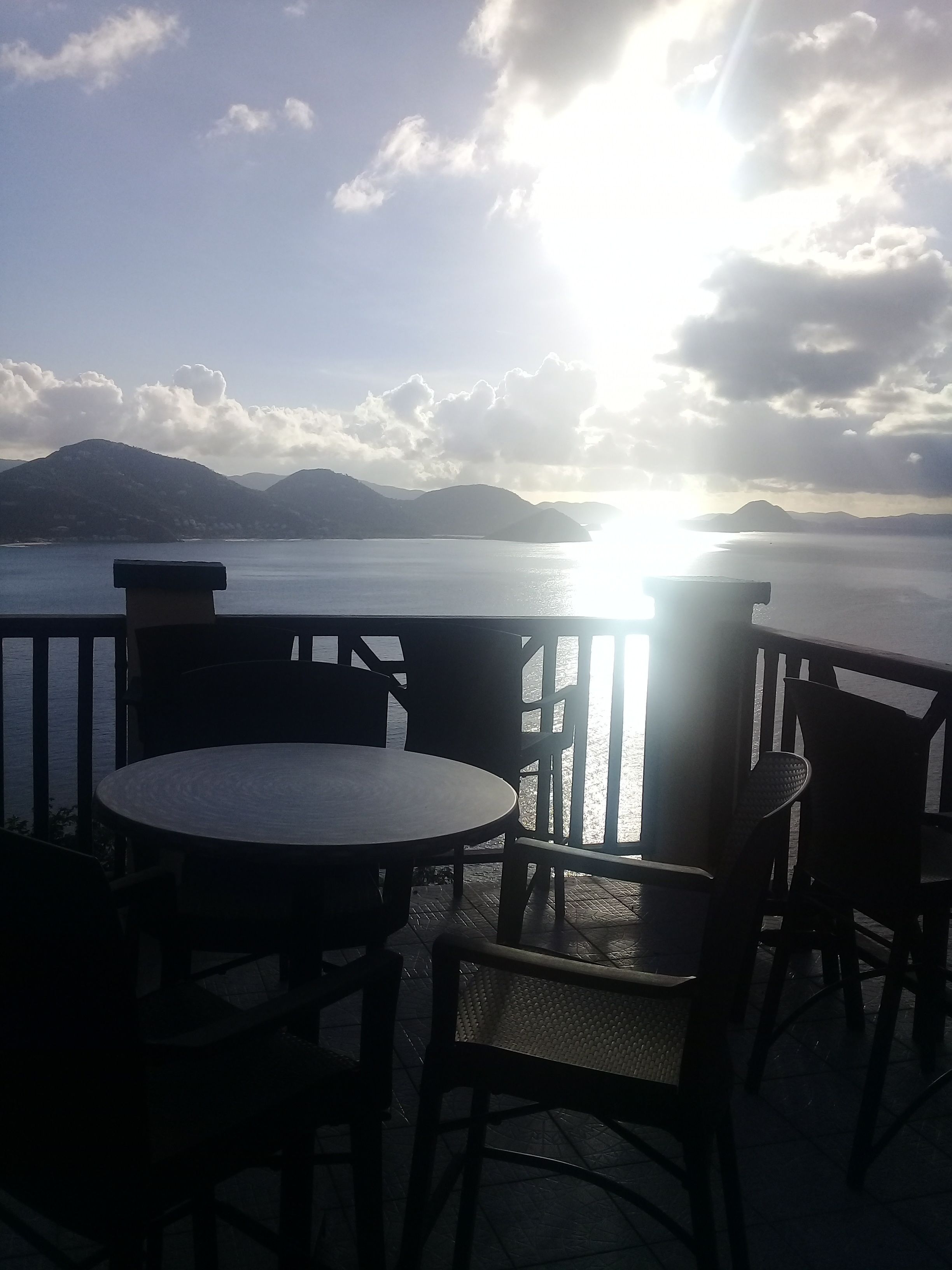 Une terrasse avec une table ronde et des chaises, donnant sur une étendue d’eau, avec des montagnes en arrière-plan.