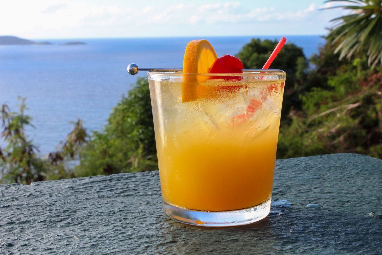 Un verre de jus d’orange avec une paille et une tranche d’orange, posé sur une table d’où l’on peut admirer l’océan.