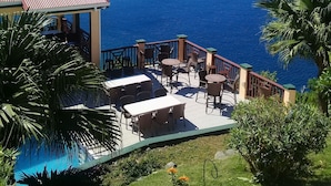 A terrace with outdoor seating overlooking a large body of water and distant landforms. - The Heritage Inn (Cane Garden Bay)