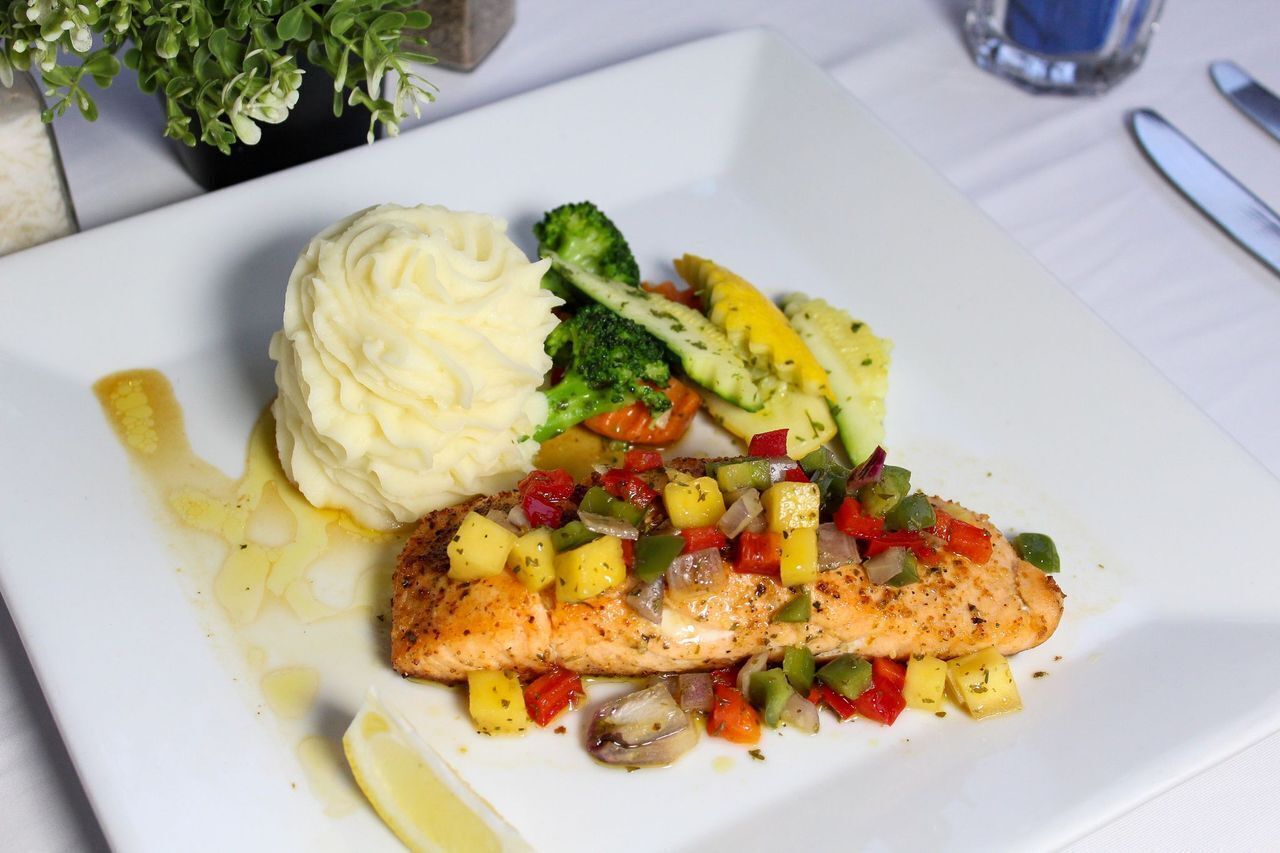 A plate with a piece of salmon, mashed potatoes, and a side of mixed vegetables.