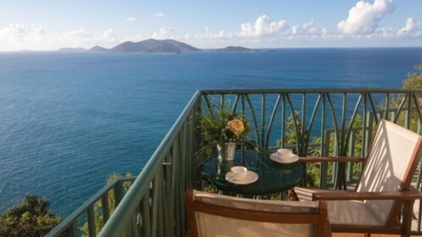 A balcony with a table and chairs overlooking a coastal view. - The Heritage Inn (Cane Garden Bay)