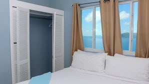 A bedroom with a bed, a window with curtains, and a view of the sea. - The Heritage Inn (Cane Garden Bay)