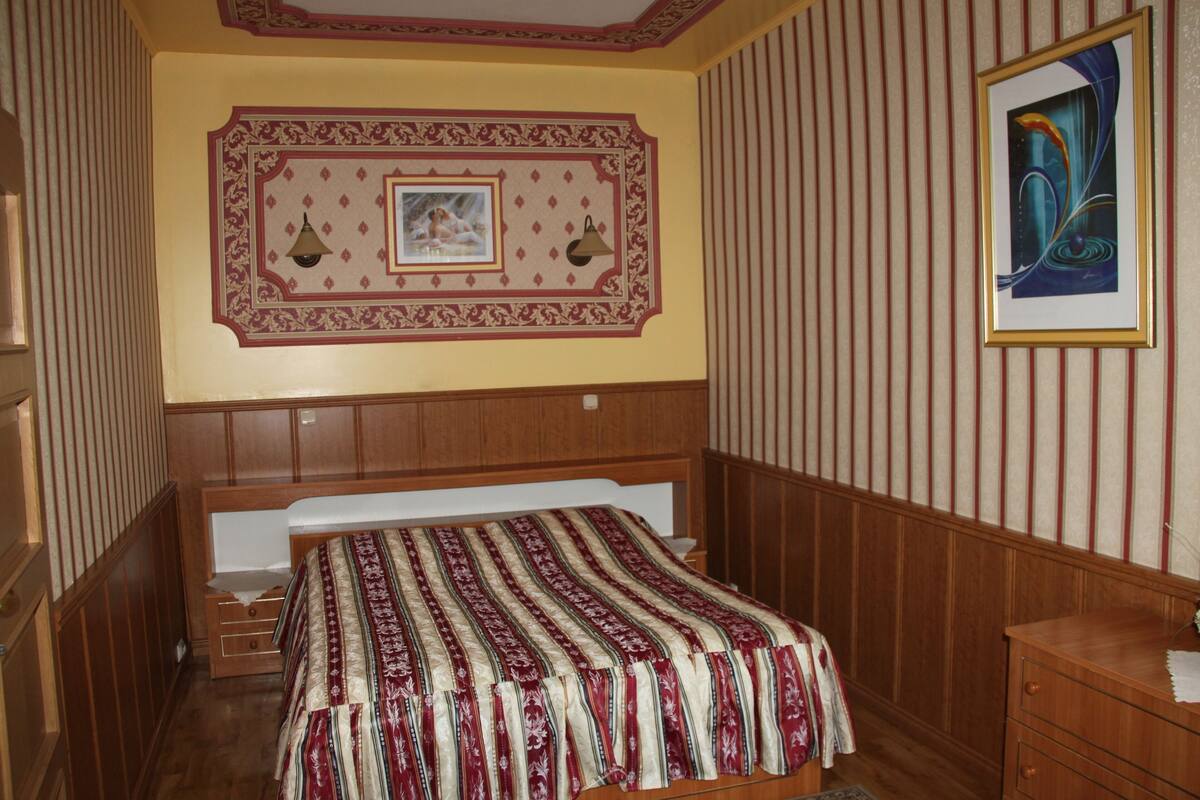 A bedroom with a wooden bed, a nightstand, a dresser, a framed picture on the wall, and a decorative ceiling medallion.