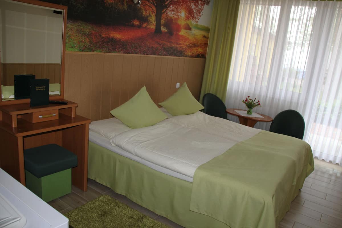A hotel room with a bed, a desk, a chair, and a small table with a vase of flowers.