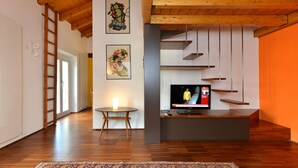 Uma sala de estar moderna com piso de madeira, uma TV sobre um móvel, uma mesa redonda e uma escada.