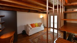 Uma sala de estar moderna com um sofá branco, vigas de madeira e uma mesa de vidro.