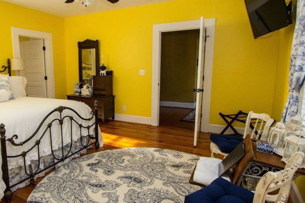 Un dormitorio con cama, cómoda, espejo, puerta y ventana con cortinas.