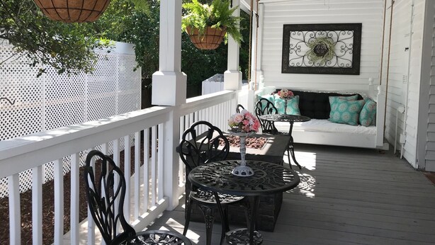 A covered porch with a white fence, a white sofa with patterned cushions, and two metal tables with chairs. - Bama Bed & Breakfast Campus (Tuscaloosa)