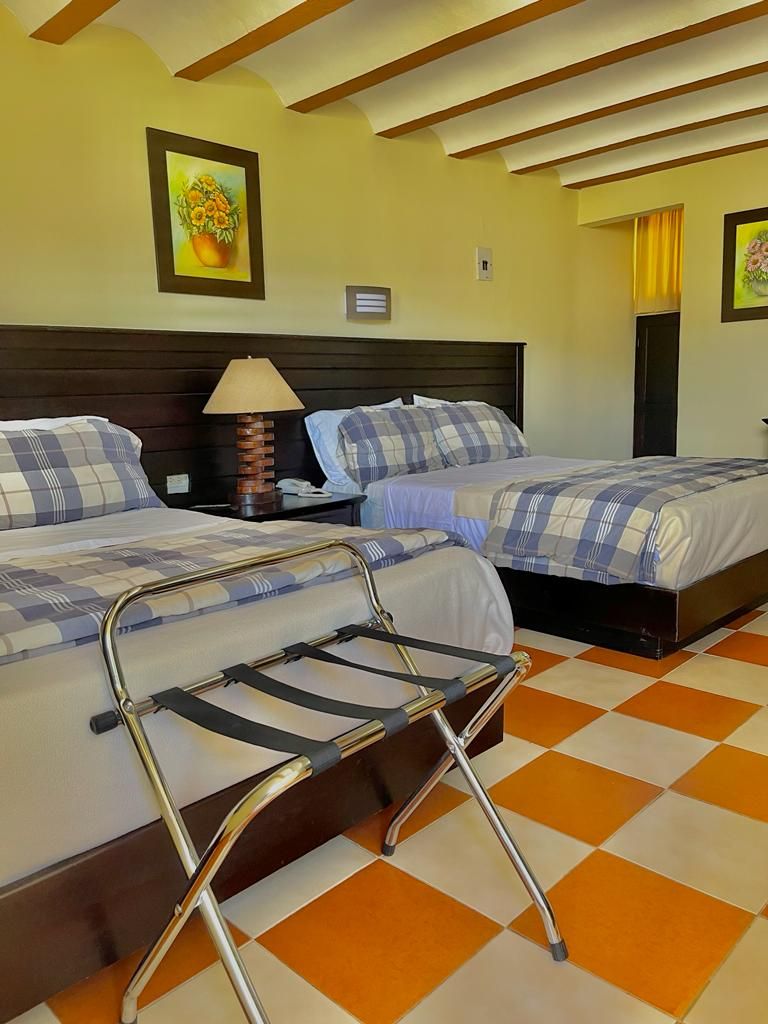 A hotel room with two beds, a metal chair, a lamp, and a checkered floor.