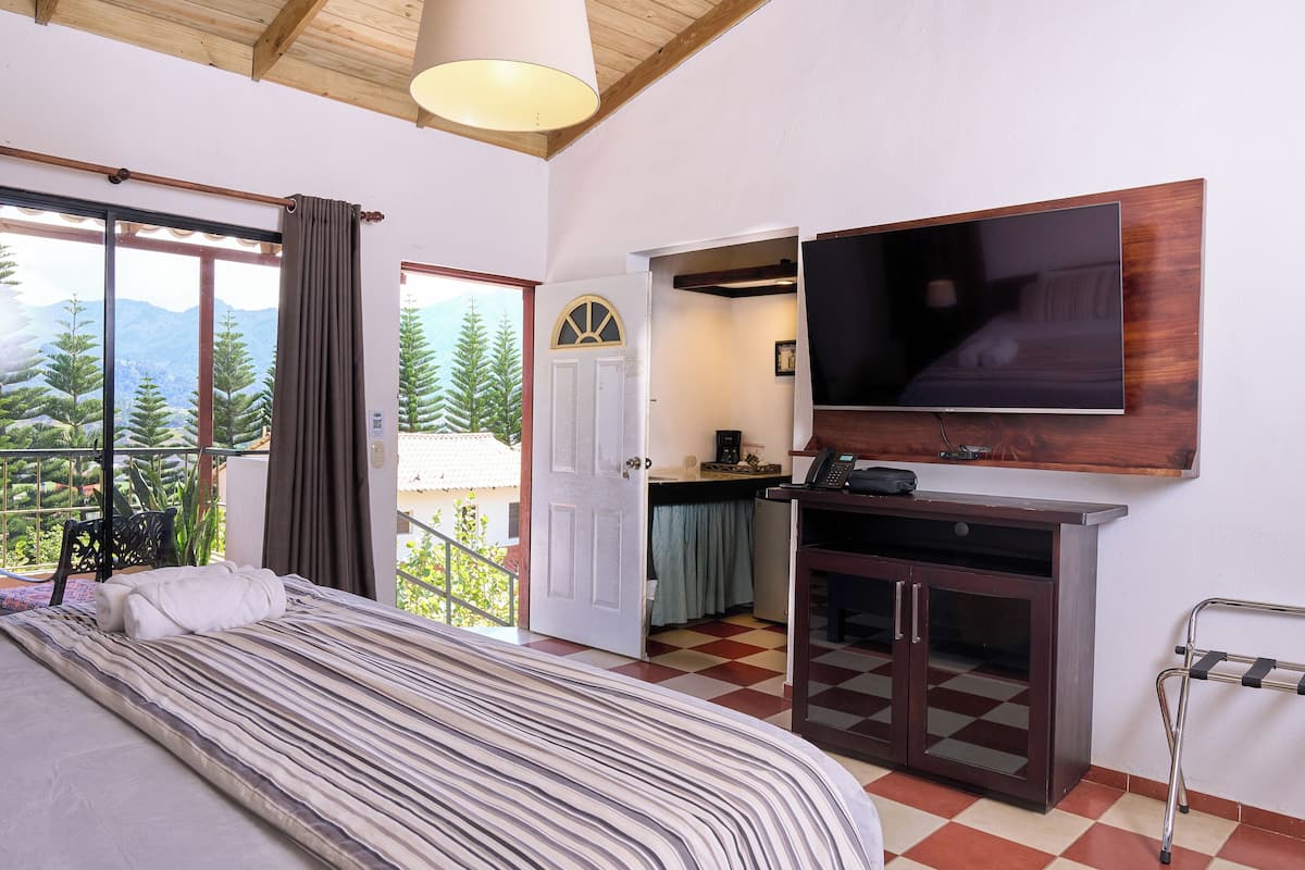 Hotelkamer met een bed, een aan de muur bevestigde televisie, een bureau met stoel en uitzicht op bomen en bergen door het raam.