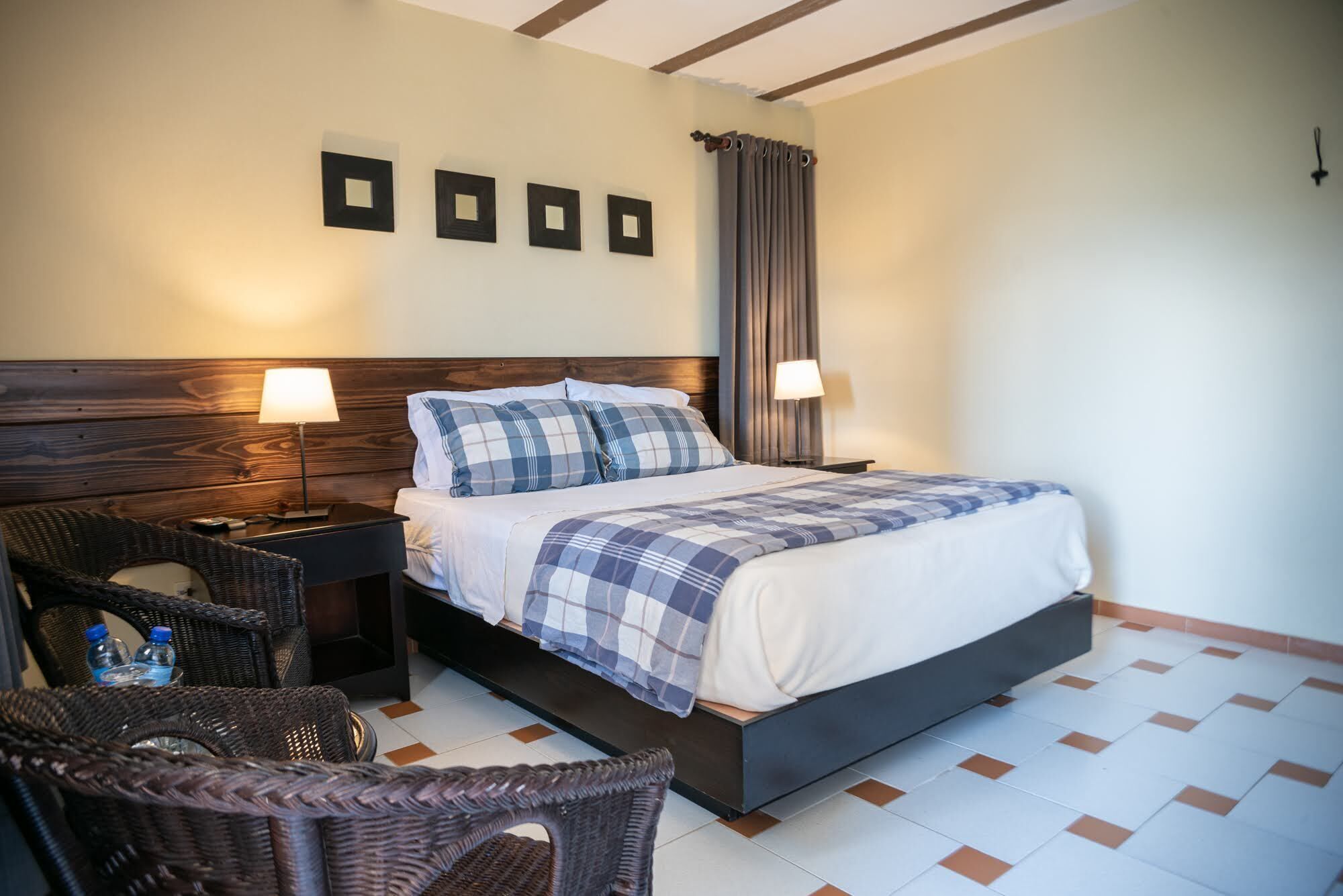 Habitación de hotel ordenada con una cama grande, dos mesitas de noche con lámparas, un cabecero y un televisor montado en la pared.