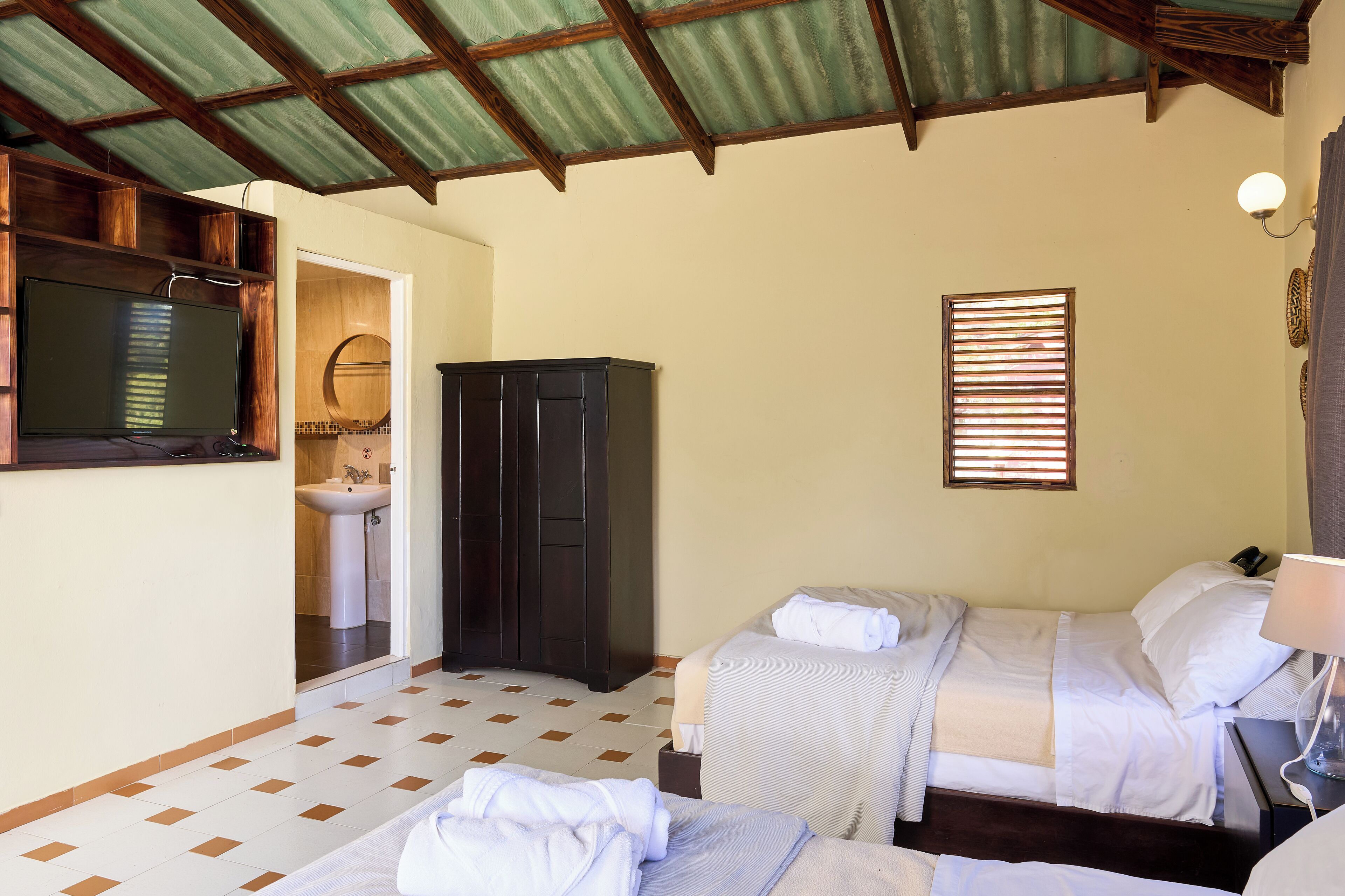 Une chambre avec deux lits, une télévision, une armoire et une salle de bain visible à travers une porte ouverte.