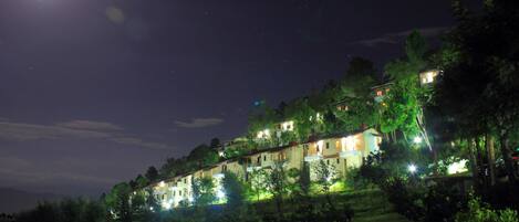 Een hotel op een helling, bestaande uit meerdere gebouwen, verlicht door kunstlicht, omgeven door bomen en groen.
