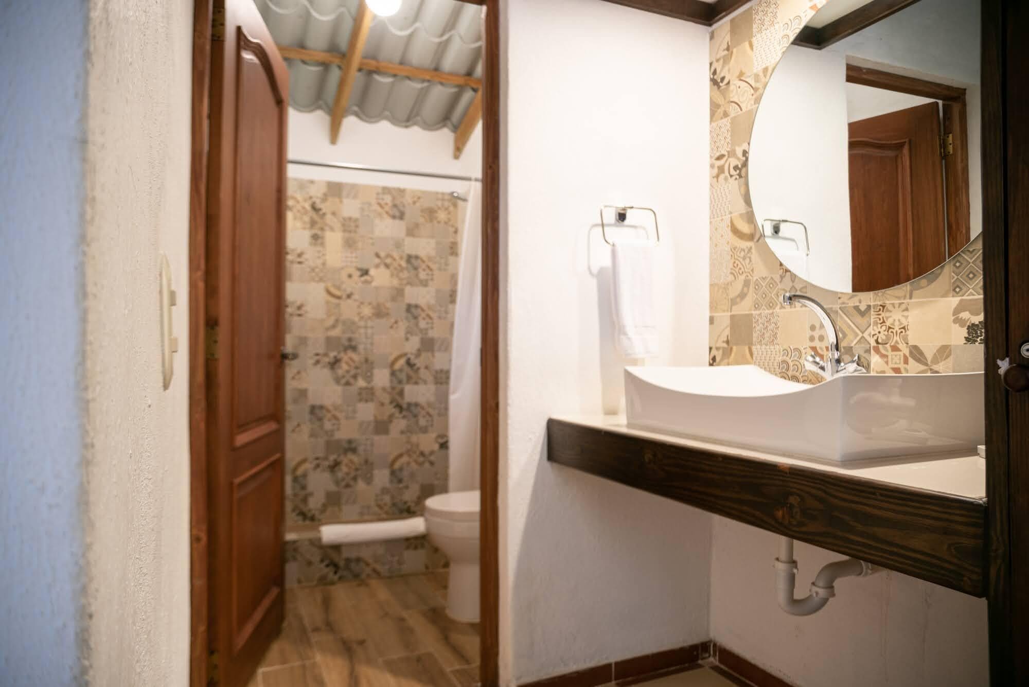 Ein Badezimmer mit Holztür, Toilette, Waschbecken mit Spiegel und Wandfliesen mit Muster.