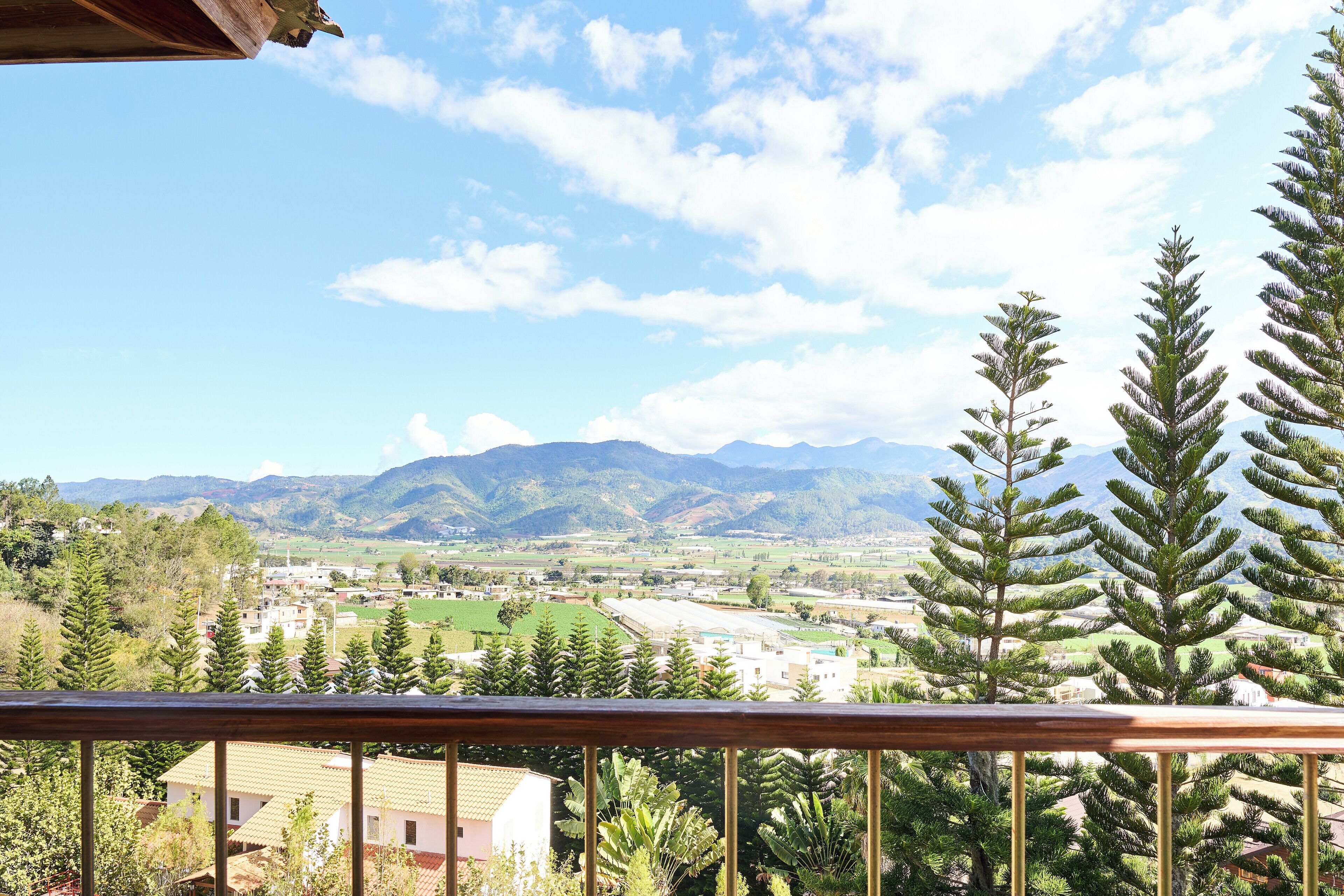 Un balcón con vistas a un paisaje montañoso, que incluye campos verdes y edificios.