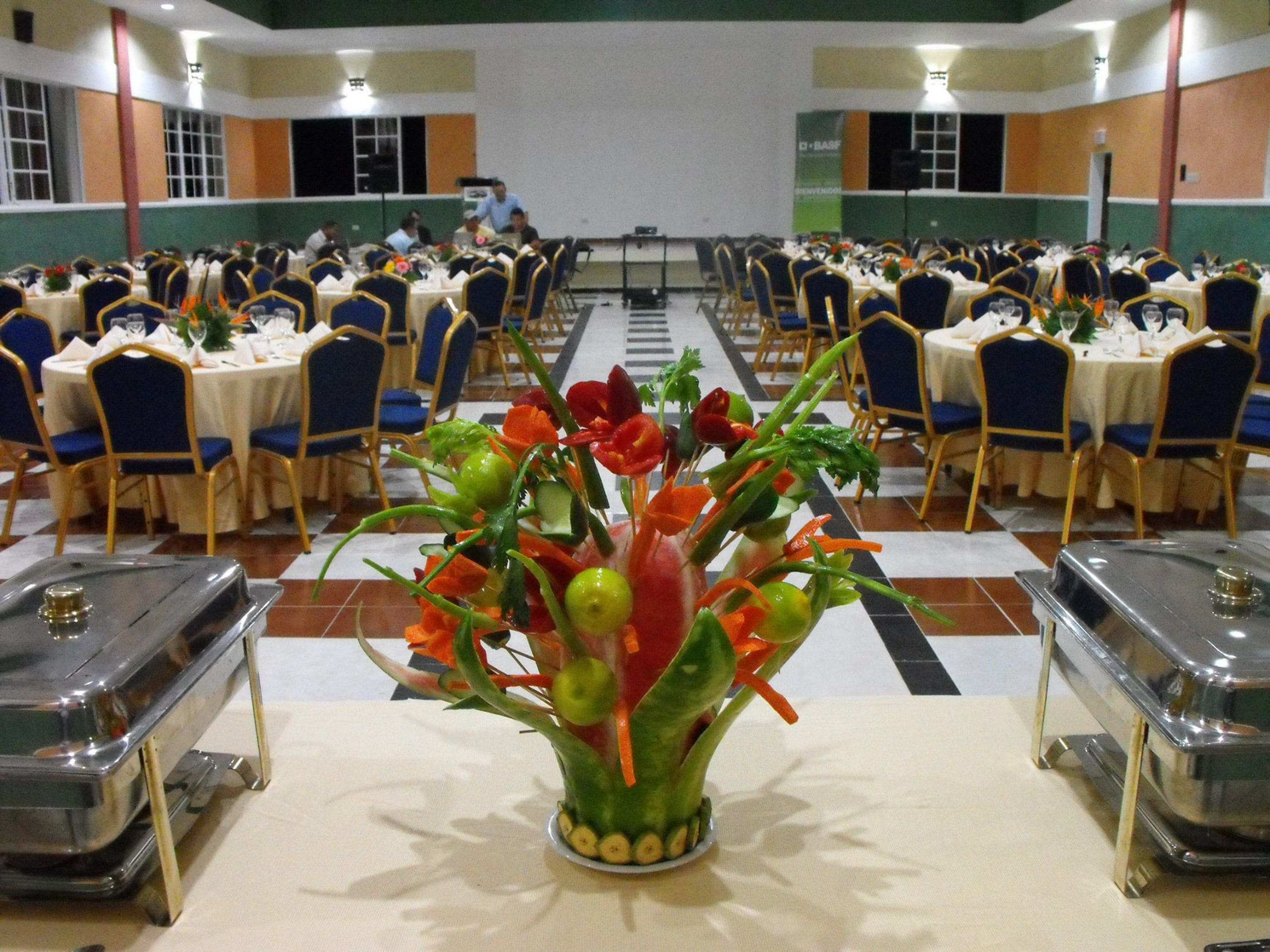 A banquet hall with round tables, blue chairs, and a central floral arrangement.