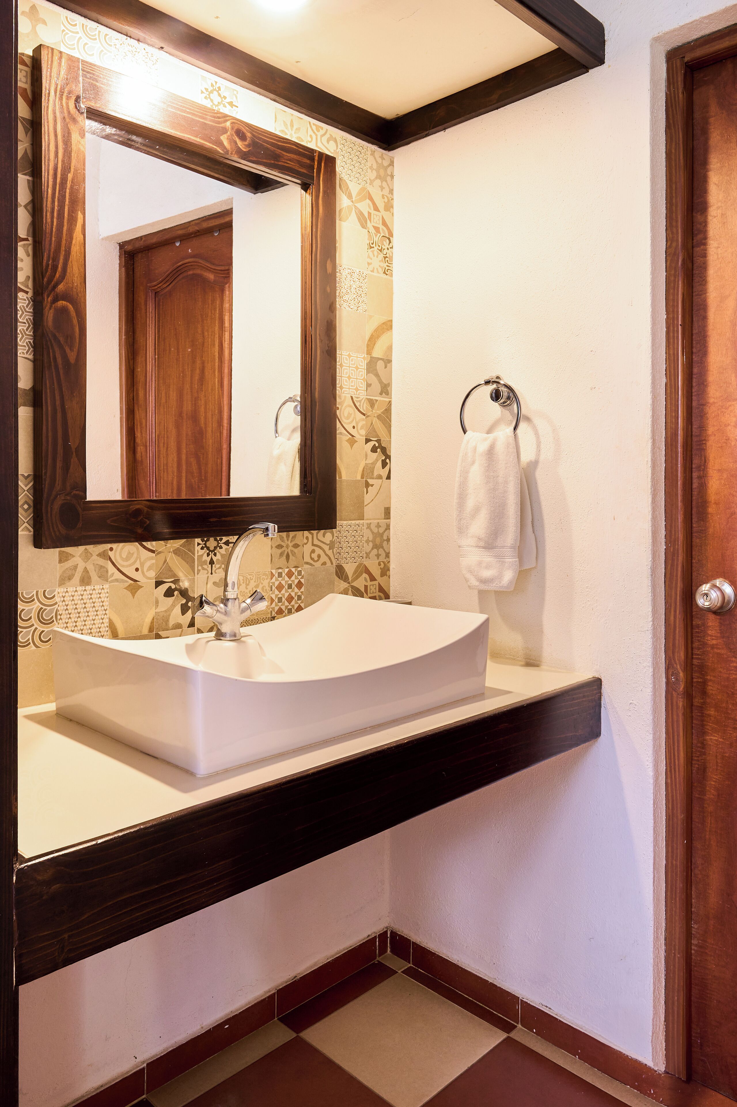 A bathroom with a white sink, a wooden-framed mirror, and a towel hanging on a ring.