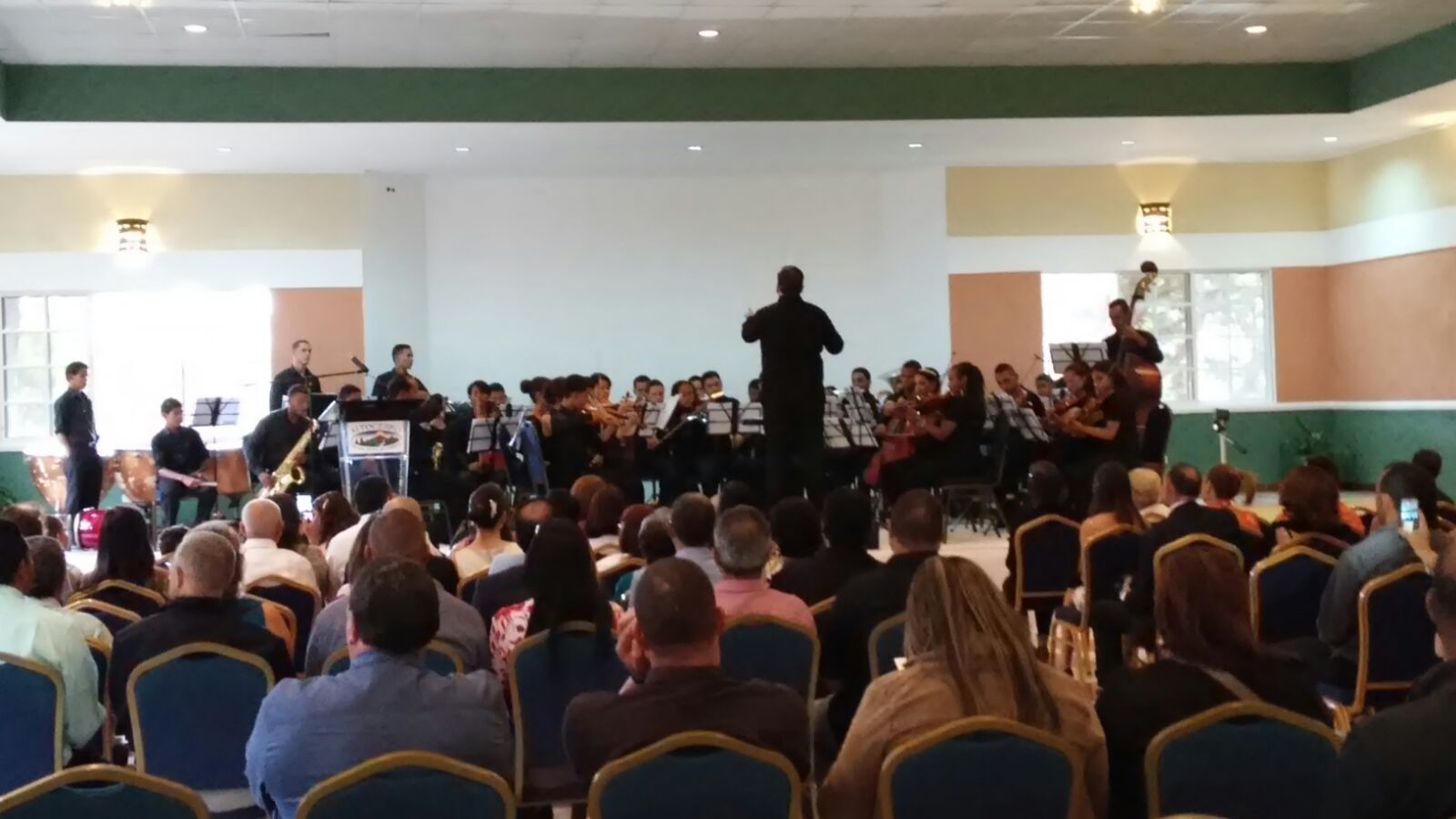 Une salle de concert où le public est assis en rangées, face à une scène où un groupe joue.