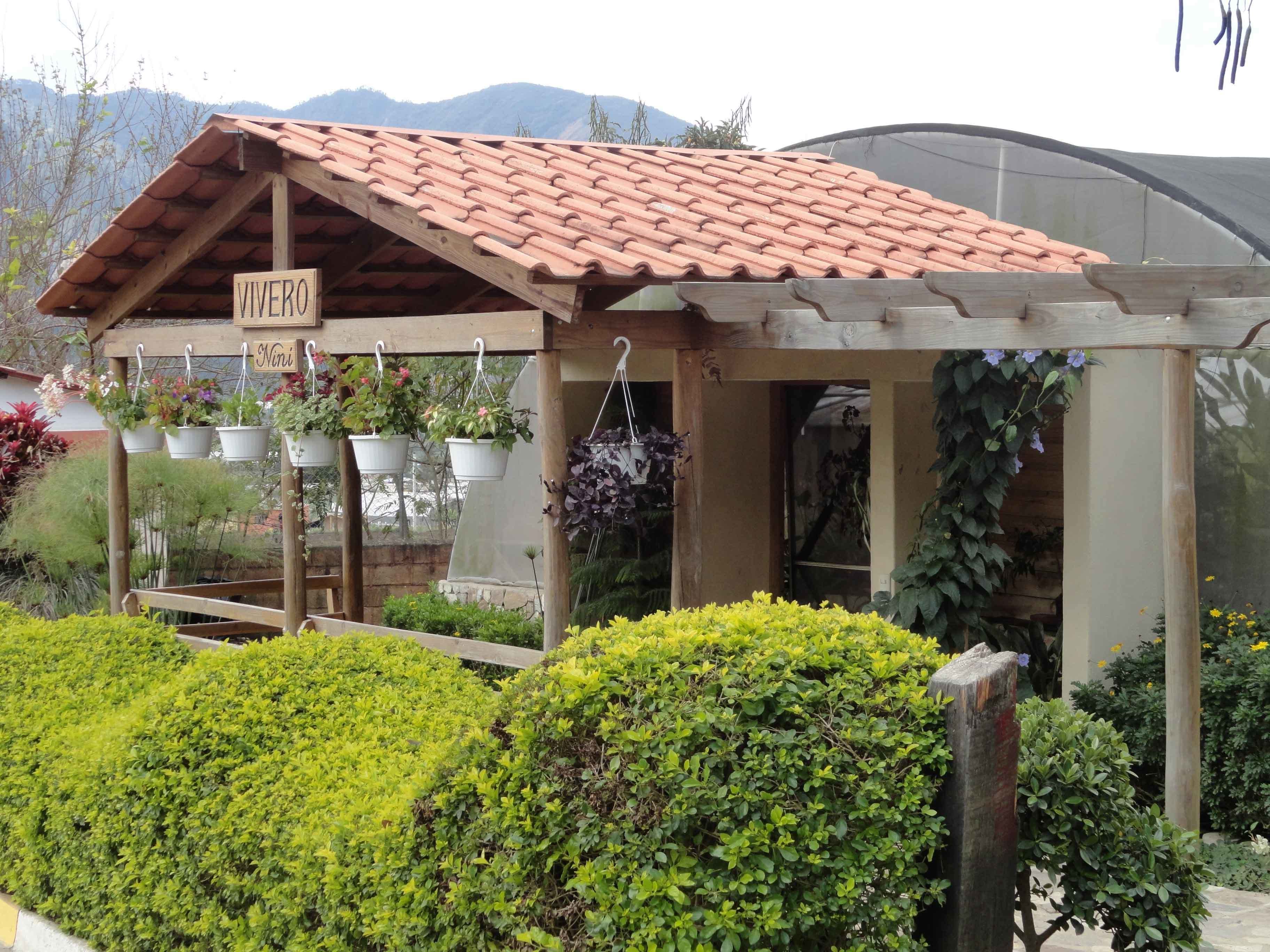 A wooden structure with a tiled roof, labeled "Vivero Nini," surrounded by well-maintained green hedges and potted plants.