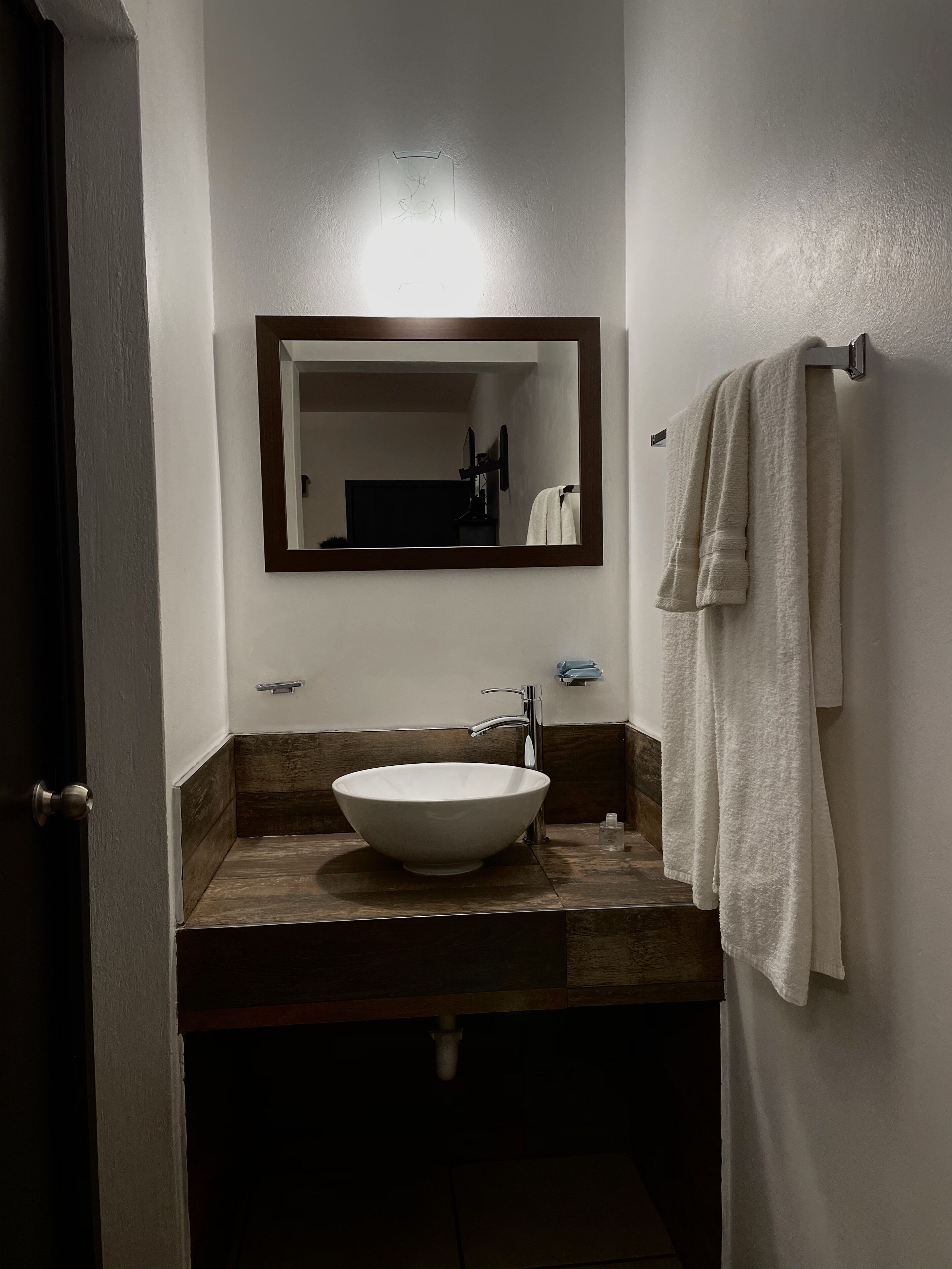Un baño con un lavamanos de pedestal, un espejo, un perchero y una puerta.