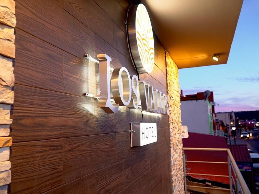 Señal de hotel con el nombre 'Los Valdos' iluminado, fachada de madera y un enchufe.