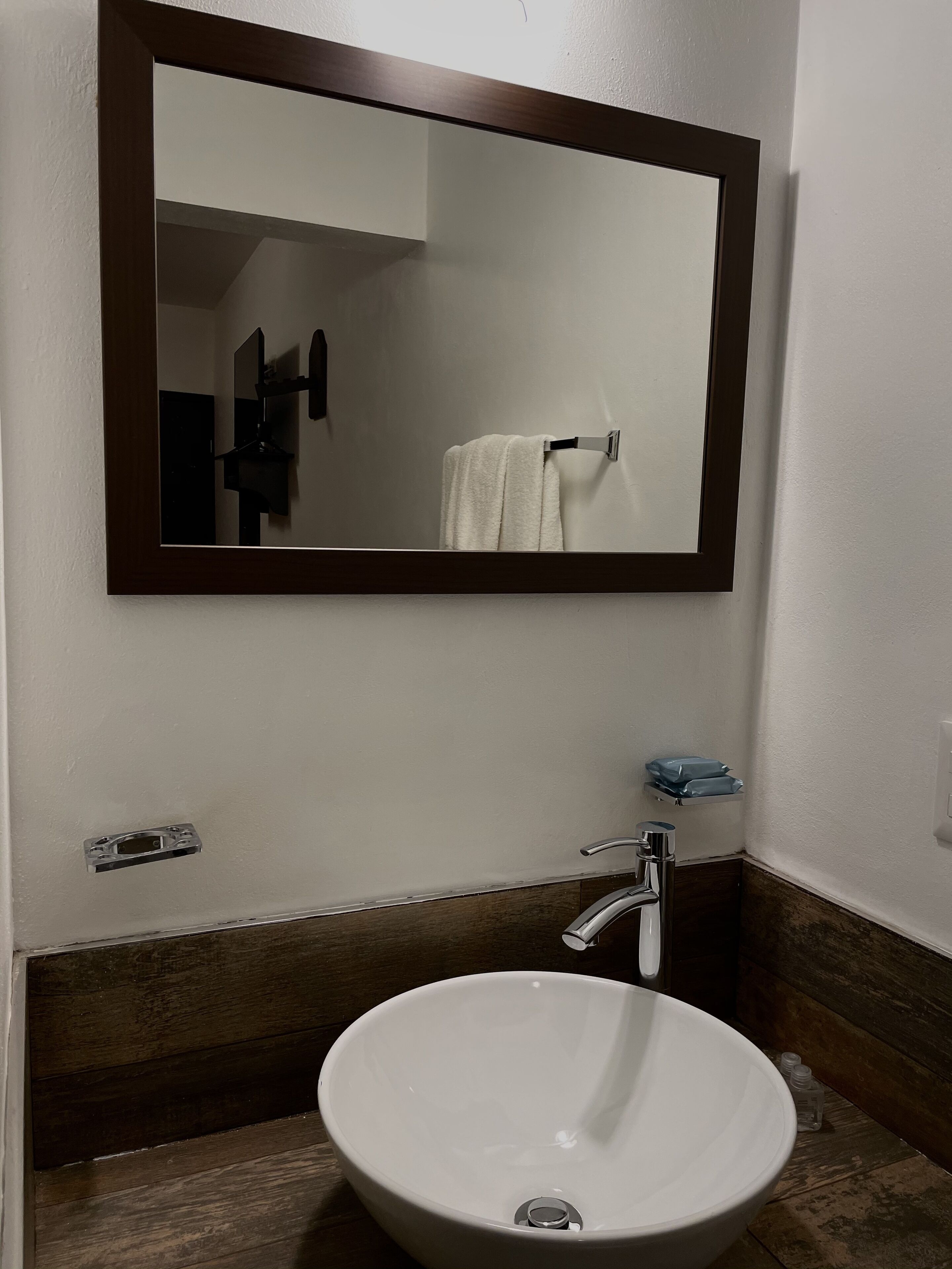 Un baño con un lavabo blanco, un espejo y una toalla colgada en un perchero.