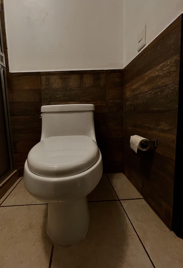 Un inodoro en un baño con paredes de madera y suelo de baldosas.