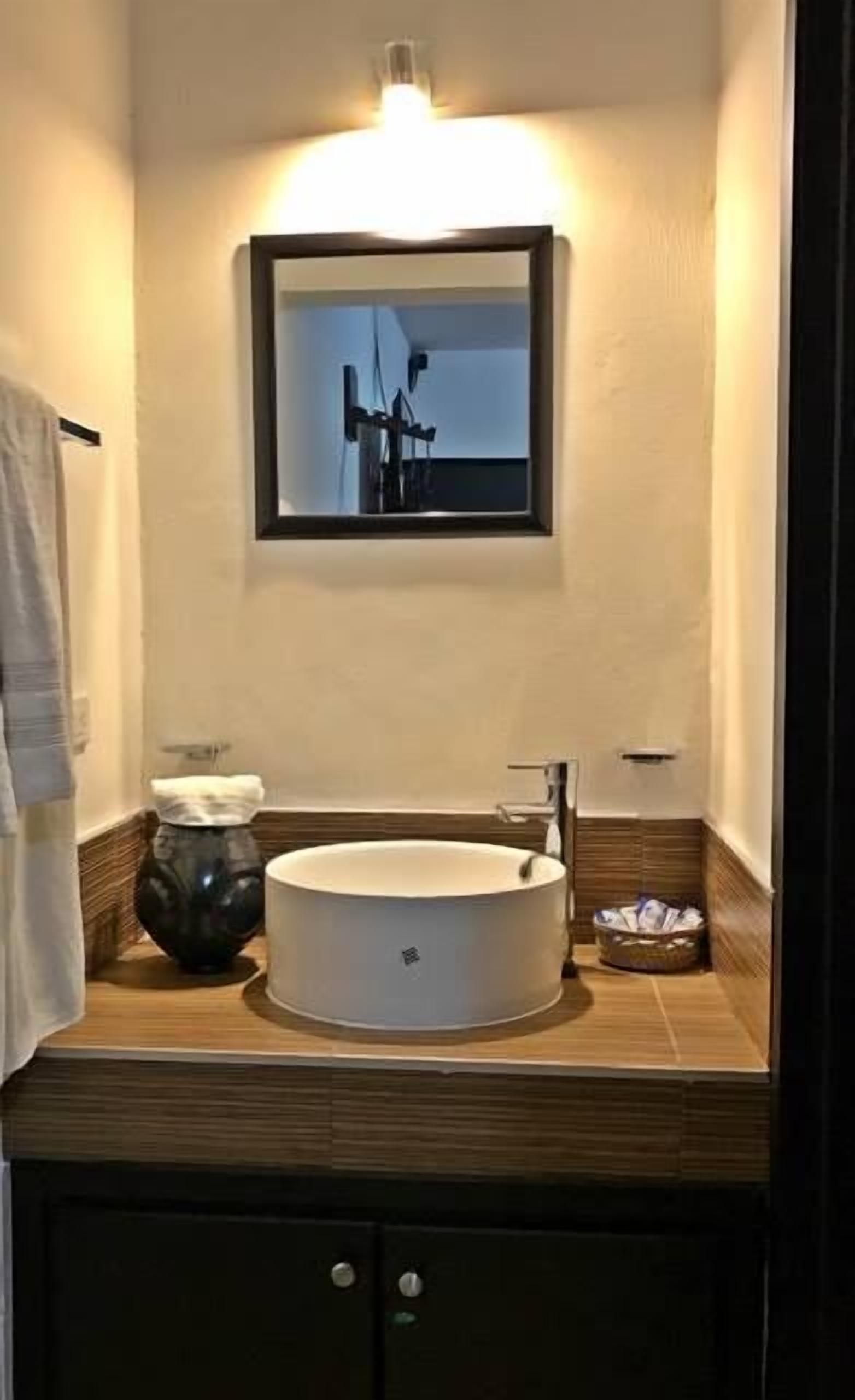 Un baño con un lavamanos redondo, un espejo y un perchero para toallas.