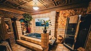 A bathroom with a large bathtub, a mirror, a potted plant, and a tiled floor. - Historic Farnsworth House Inn (Gettysburg)