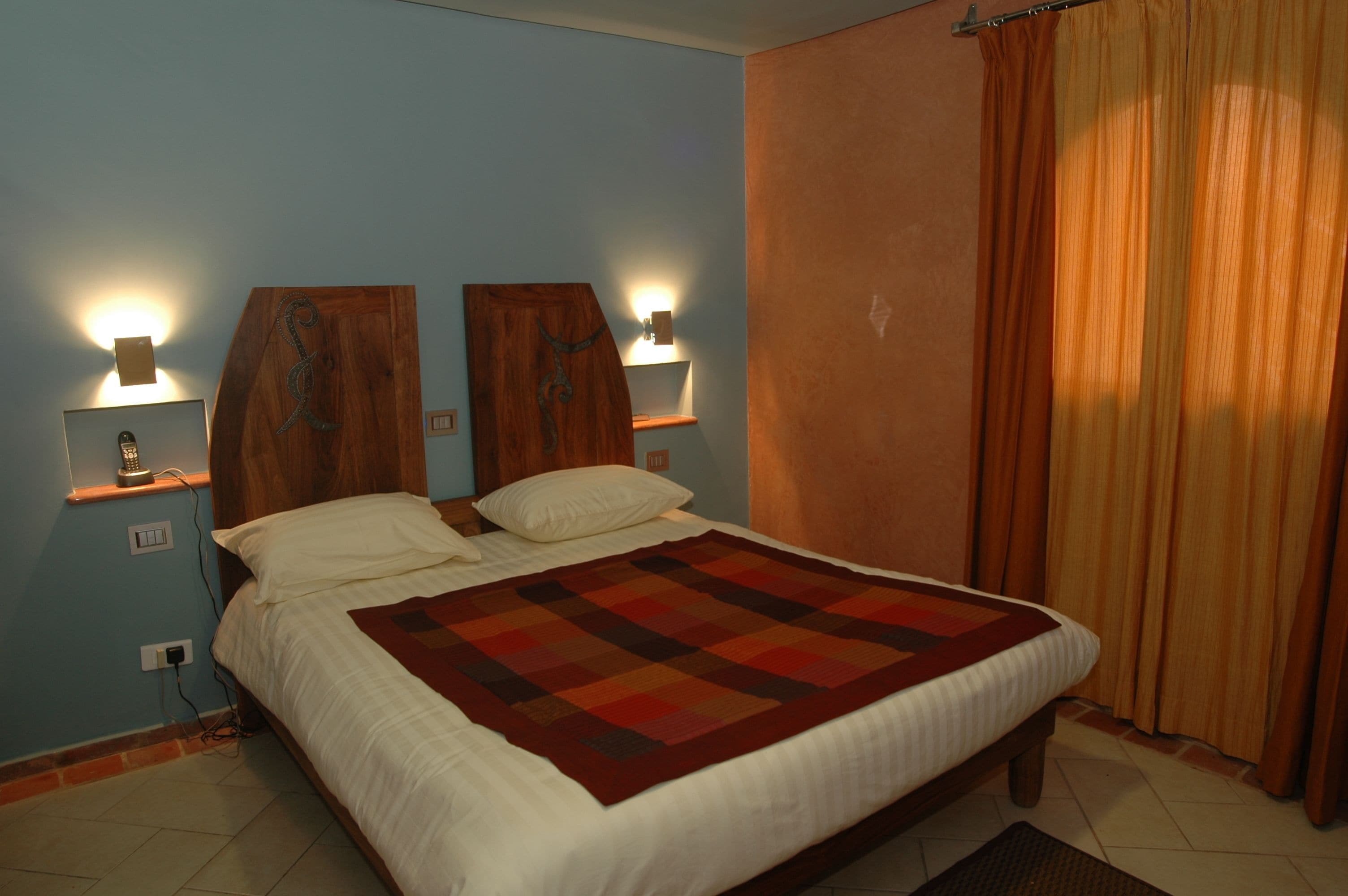 A bedroom with a bed, two wall-mounted lamps, a wooden headboard, and a window with curtains.