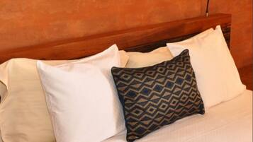 A bed with white and patterned pillows, a wooden headboard, and a wall-mounted light fixture.