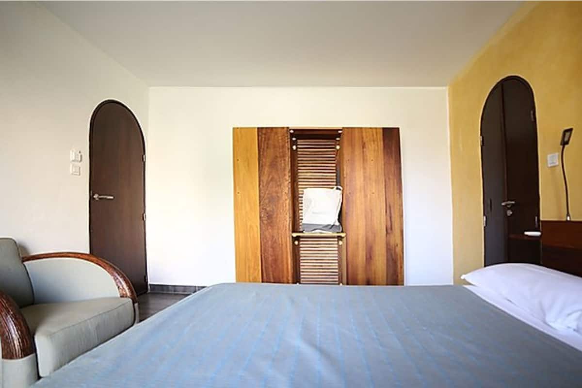 A hotel room with a bed, a chair, and a wardrobe with a mirror.