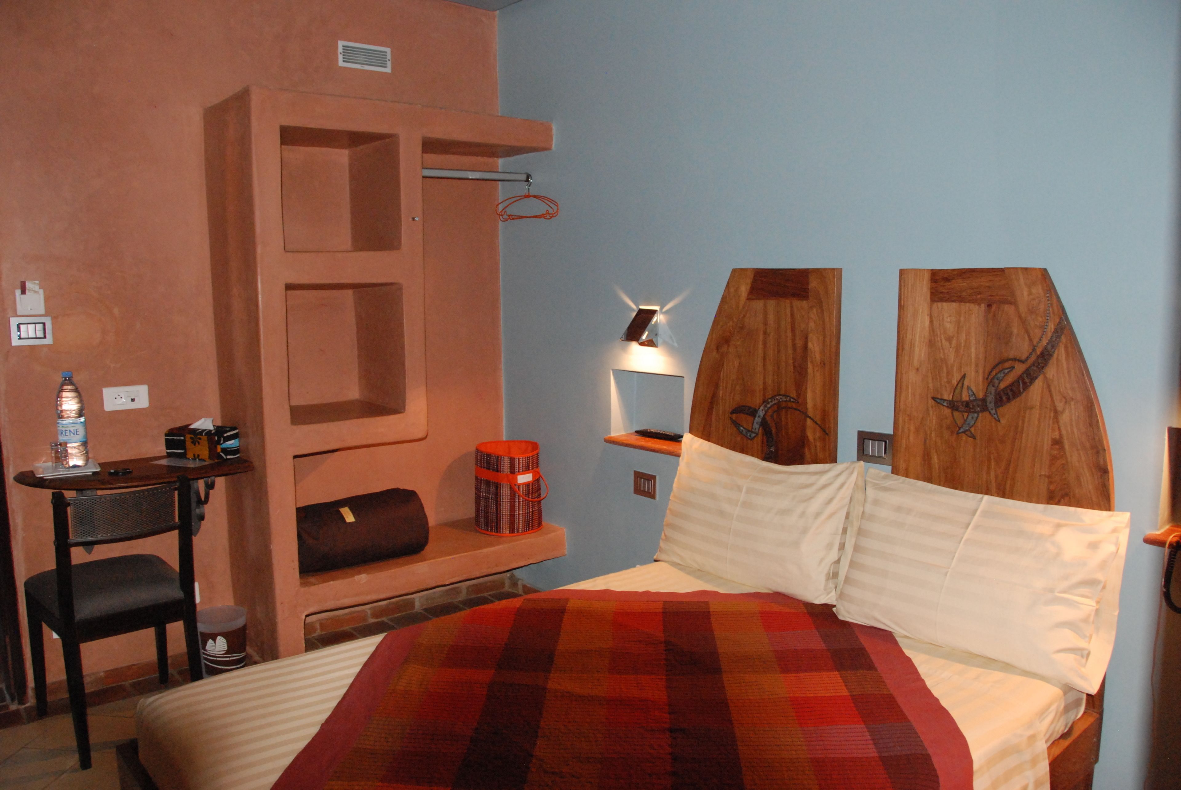 Una habitación de hotel con cama, escritorio, silla, mesita de noche y estante en la pared.